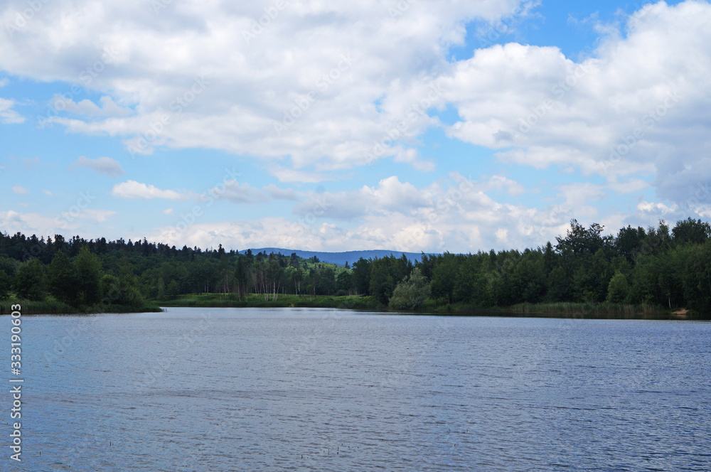 Mountain lake with cold dark water surrounded by green forest under a blue sky on a sunny day