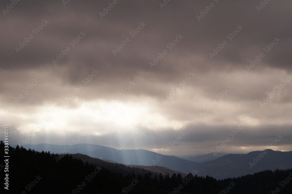 View of autumn mountains with trees without leaves under a cold gray sky and heavy white clouds
