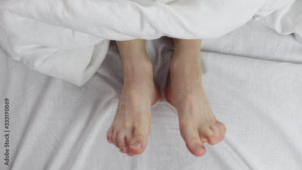 naked beautiful legs under a white blanket. both legs were under the covers. naked beautiful legs under a white blanket. both legs were under the covers.