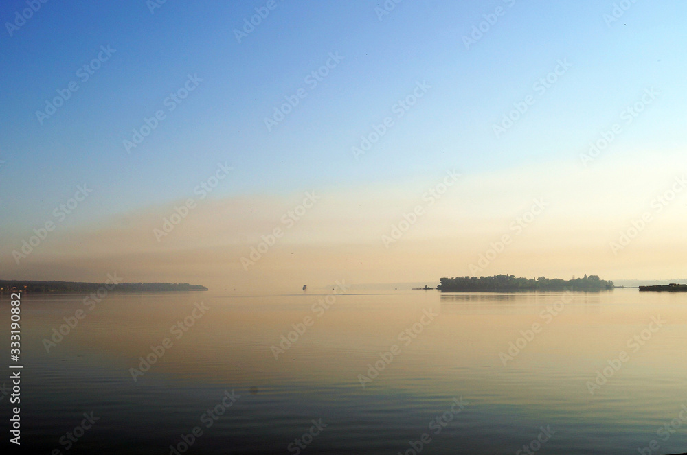 View of the lake with mirrored calm water covered in fog on a cool summer morning
