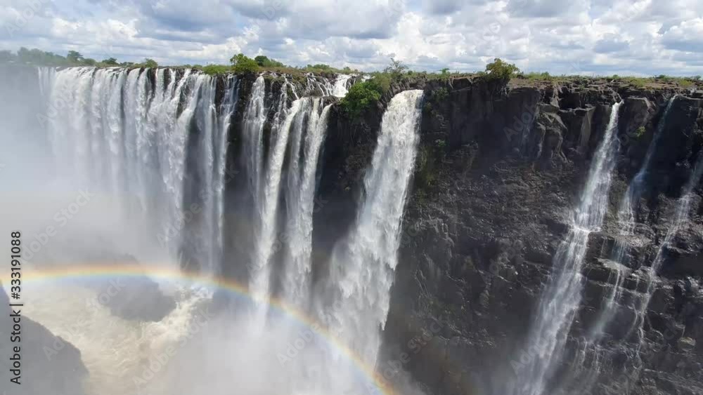 Rainbow over Victoria Falls at the Zambia Zimbabwe boarder with blue sky and white clouds and water cascading over the cliff. Rainbow over Victoria Falls at the Zambia Zimbabwe boarder with blue sky and white clouds and water cascading over the cliff.