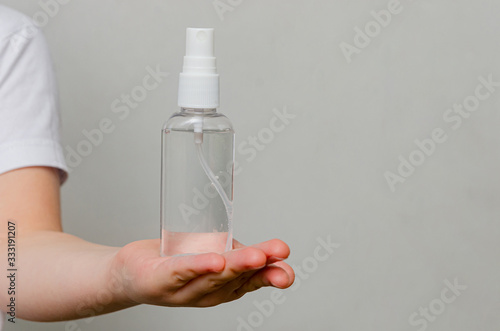Hands of a child of four years holding a bottle with a sanitizer on a gray background