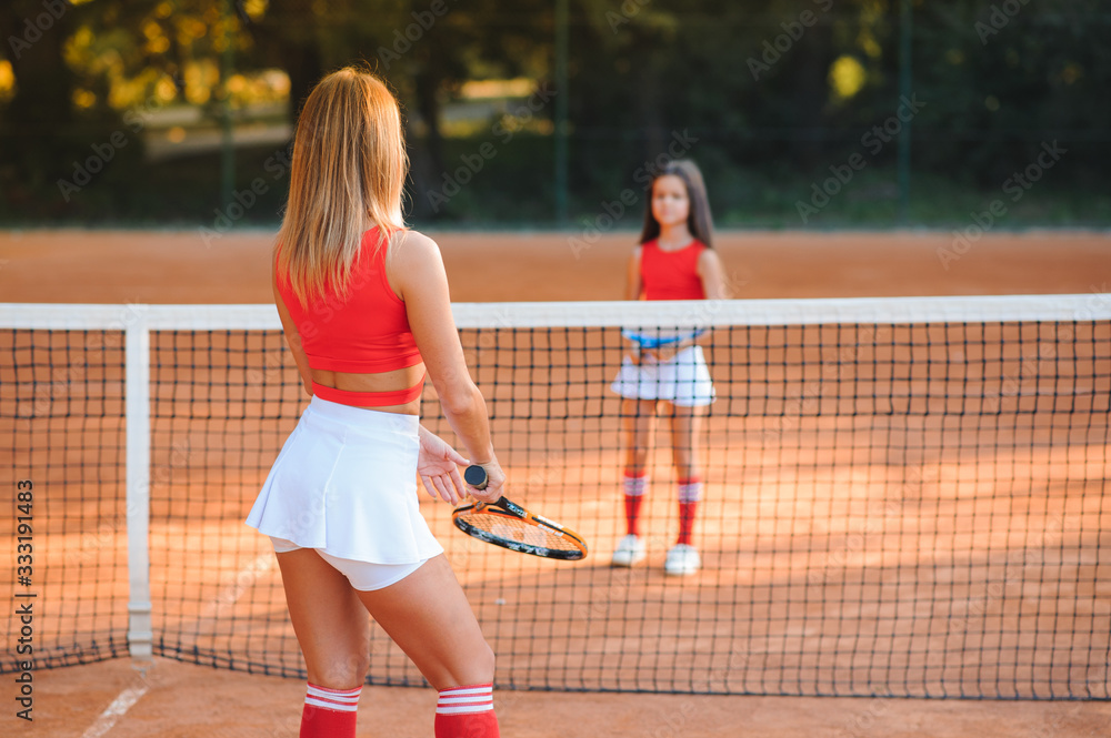 Obraz premium Little girl and her mother playing tennis on court