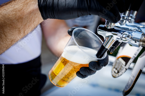 Quadro su tela Bartender in black gloves pours beer into a disposable plastic glass