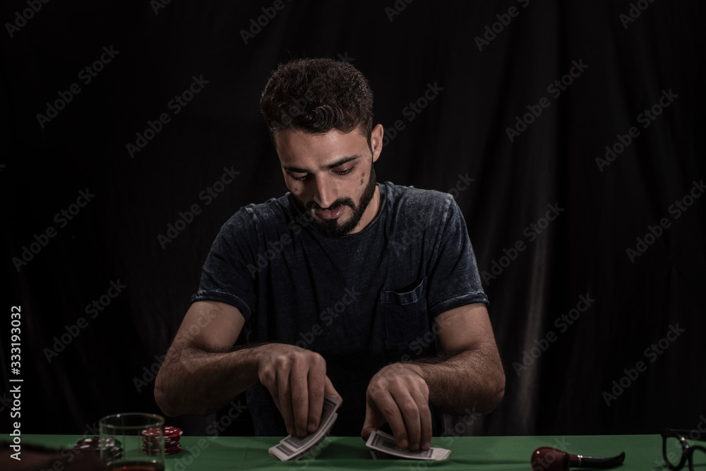 Portrait of young brunette Indian/European/Arabian/Kashmiri man in casual tee shirt throwing casino chips on a casino table in black copy space studio background. lifestyle and fashion. Portrait of young brunette Indian/European/Arabian/Kashmiri man in casual tee shirt throwing casino chips on a casino table in black copy space studio background. lifestyle and fashion.