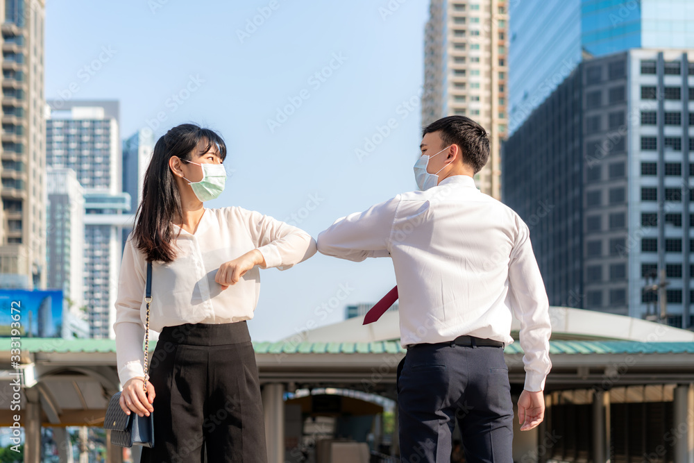 Elbow bump is new novel greeting to avoid the spread of coronavirus. Two Asian business friends meet in front of office building. Instead of greeting with a hug or handshake, they bump elbows instead. Elbow bump is new novel greeting to avoid the spread of coronavirus. Two Asian business friends meet in front of office building. Instead of greeting with a hug or handshake, they bump elbows instead.