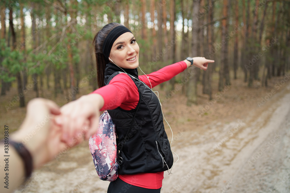 Beautiful teenager leading way, holding boyfriend's hand, smiling with joy, taking him to a nature adventure, outdoors trekking or hiking trip. Follow me concept. 
