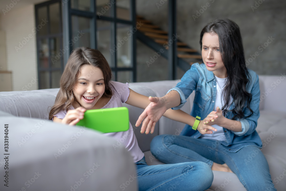 Dark-haired mom trying to take smartphone from her daughters hands Dark-haired mom trying to take smartphone from her daughters hands
