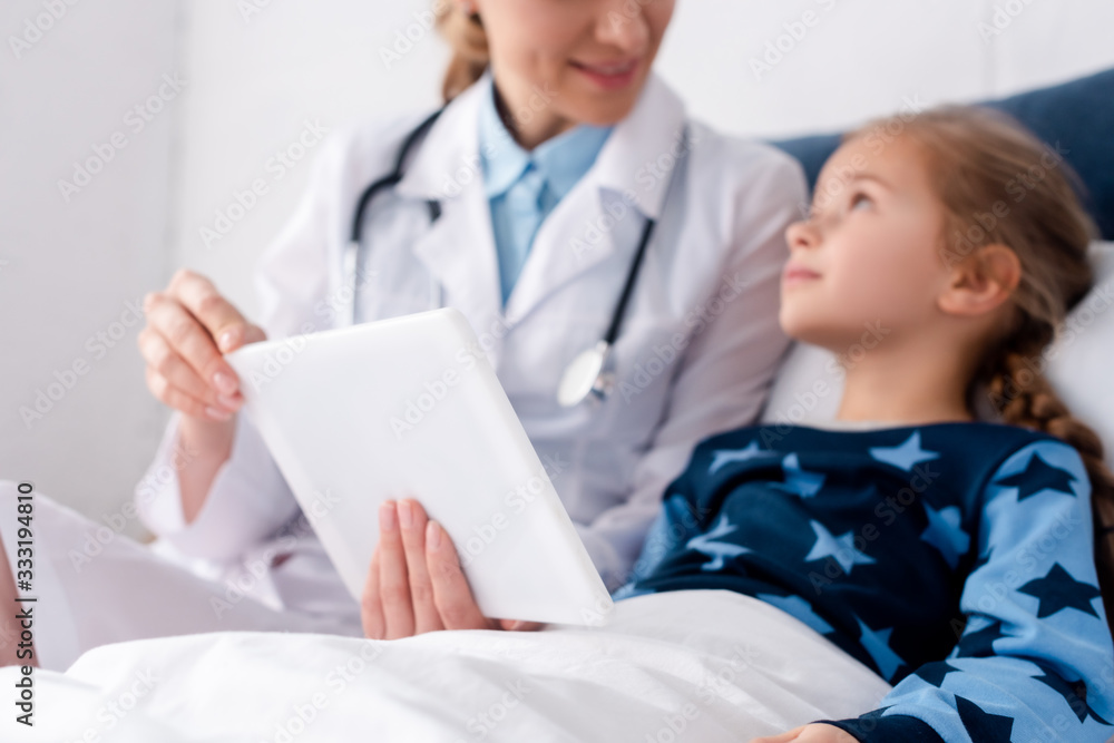 selective focus of doctor in white coat holding digital tablet near sick kid selective focus of doctor in white coat holding digital tablet near sick kid