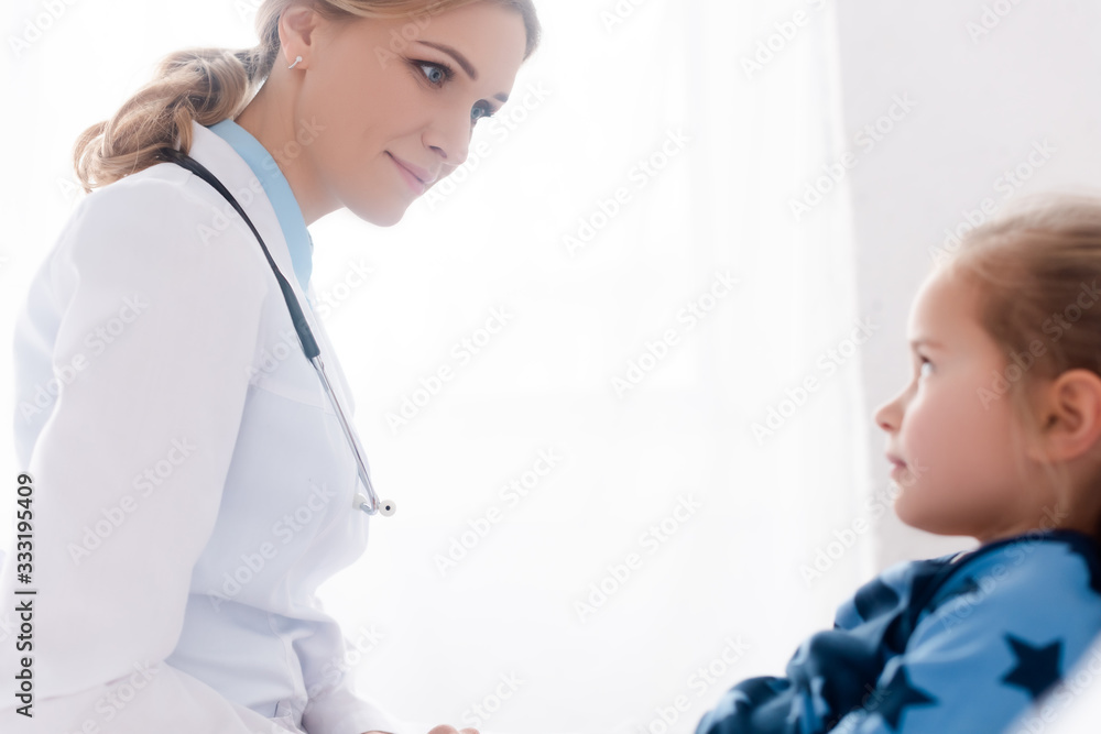 selective focus of attractive doctor in white coat looking at sick kid selective focus of attractive doctor in white coat looking at sick kid