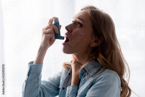 asthmatic woman touching neck and using inhaler