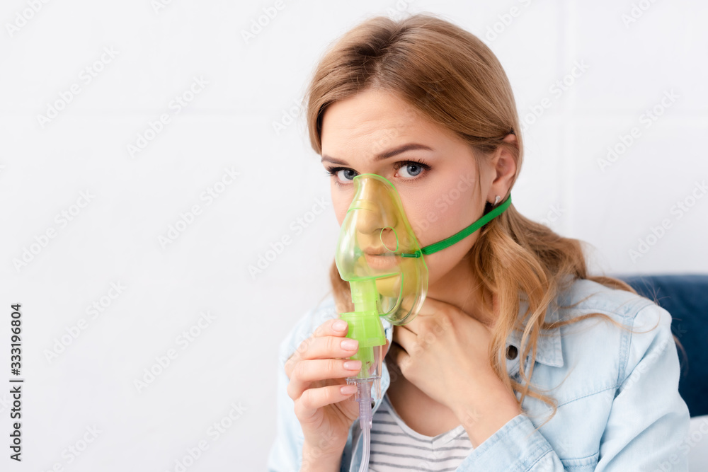 asthmatic woman holding respiratory mask near face and looking at camera