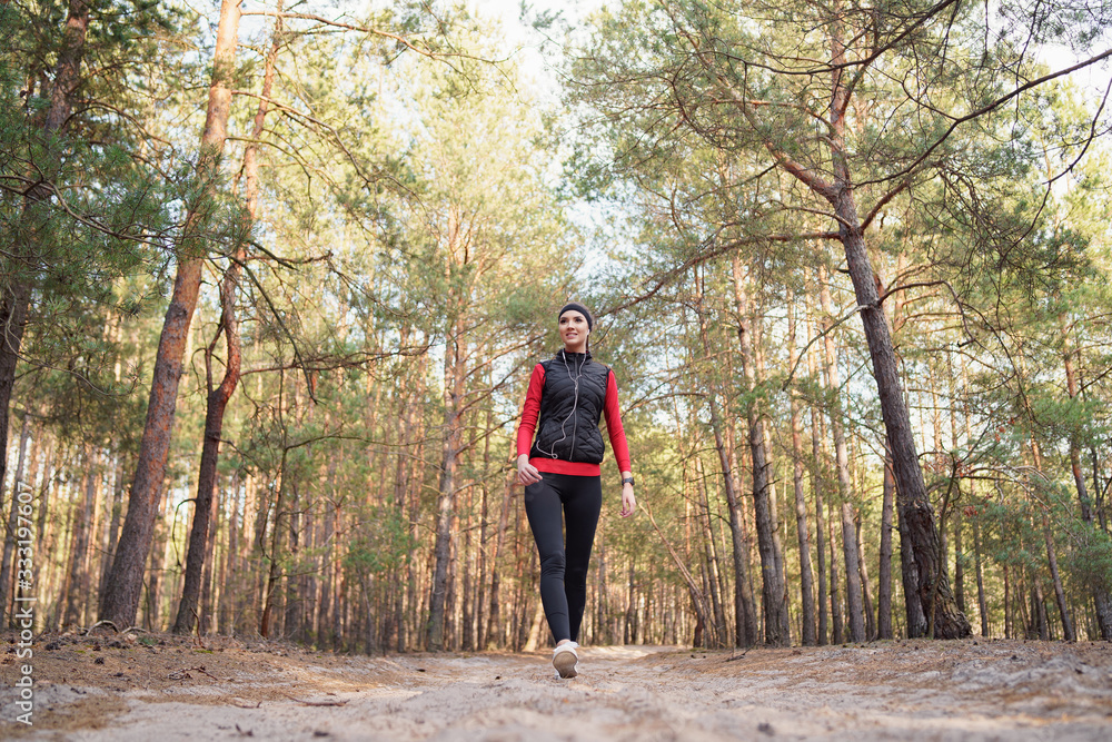 Happy teenage girl is walking in a pine forest at the weekend. She is listening  favorite music. She has a beautiful smile. Healthy lifestyle and relax concept. Freedom.