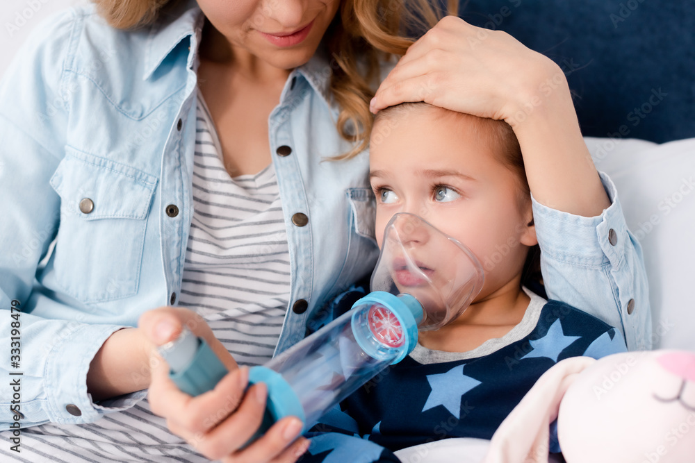 caring mother holding inhaler with spacer near sick daughter caring mother holding inhaler with spacer near sick daughter