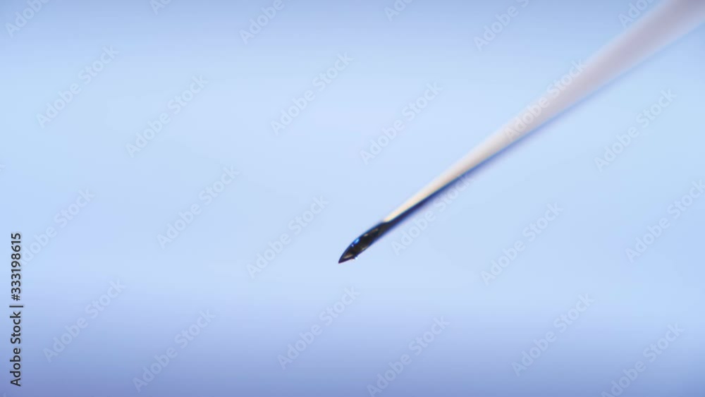 Shiny spots of medical liquid falling from a metallic needle put askew in a lab Shiny spots of medical liquid falling from a metallic needle put askew in a lab