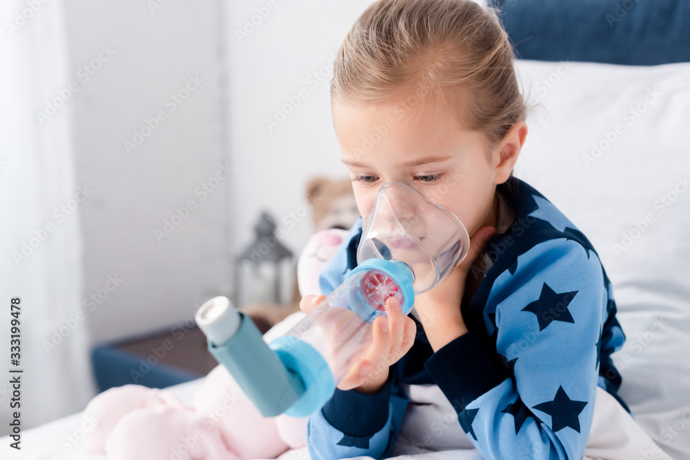 Fototapeta premium sick child using inhaler with spacer in bedroom