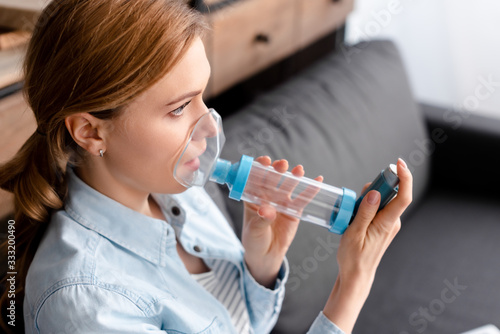 Photos asthmatic woman using inhaler with spacer in living room