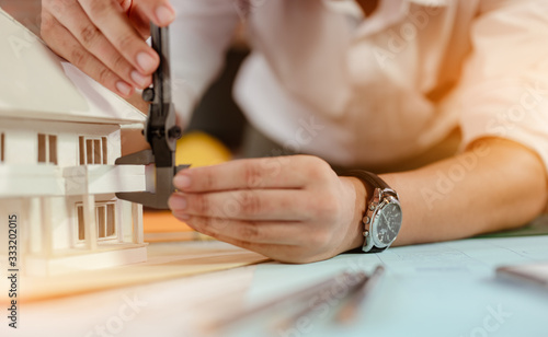 Close up of male architect hands measuring and making model house on the desk at sunset. Engineer  Engineering  Architecture  Design  Planning  Occupation concept.