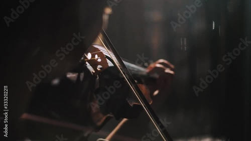 Young woman fiddler practice playing the violin at home in harsh daylight, low light scene, detail of instrument in moody scene, focus on bridge and bow