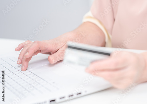 Close up hands of an old woman hold credit card and use laptop. Online shopping
