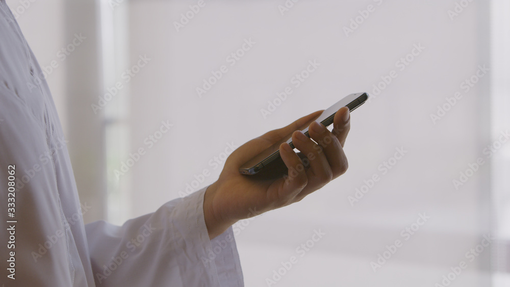 man wearing a thawb reading from a smartphone