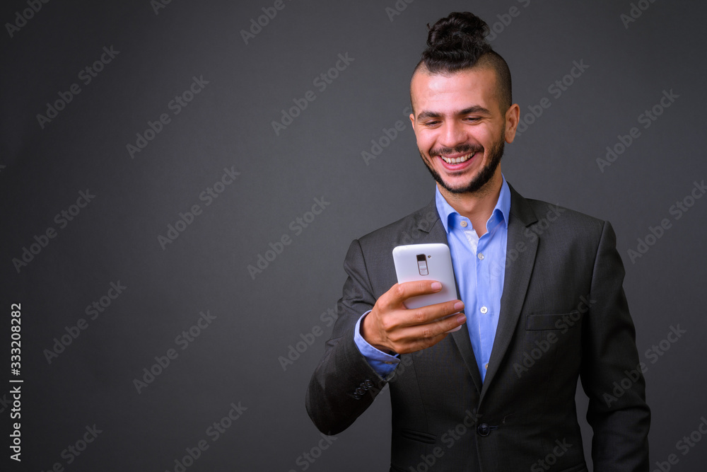 Portrait of happy bearded Turkish businessman in suit using phone Portrait of happy bearded Turkish businessman in suit using phone