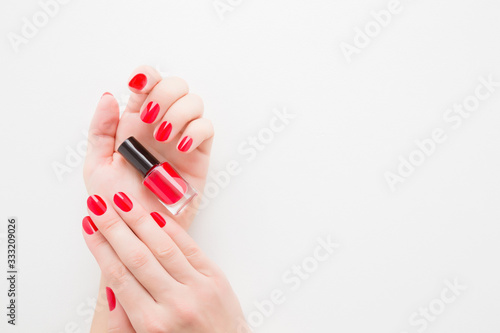 Beautiful groomed woman fingers with red nails on white table background. Hands holding bottle of nail polish. Closeup. Manicure, pedicure beauty salon concept. Empty place for text or logo. Top view.