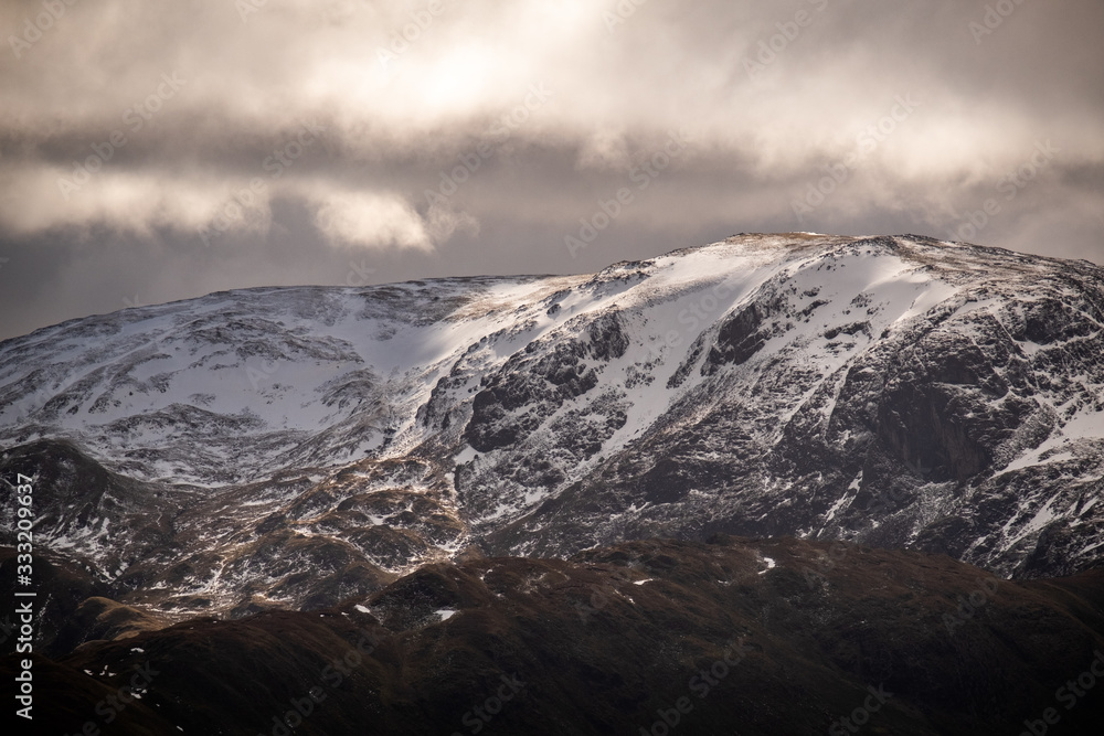 Sun breaking through clouds on the snow covered Eastern Face of Dolywaggon Pike, Lake District, UK