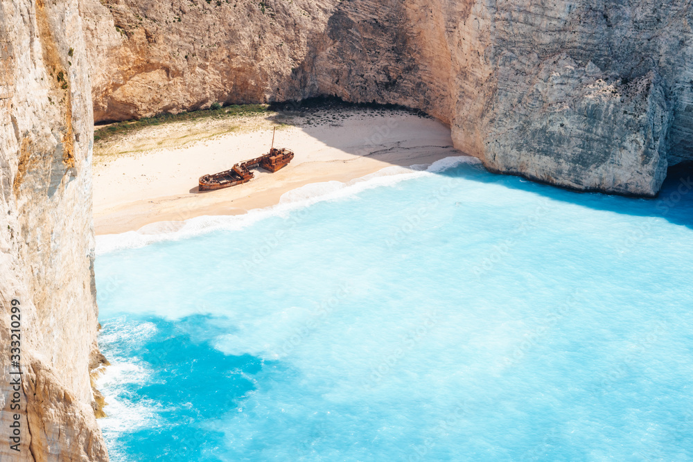 Empty Navagio beach. Turquoise blue sea cove surrounded by huge white limestone cliffs on sunny day. Famous landmark location on Zakynthos island, Greece