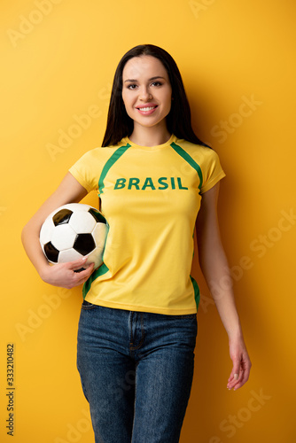 smiling female football fan holding ball on yellow © LIGHTFIELD STUDIOS
