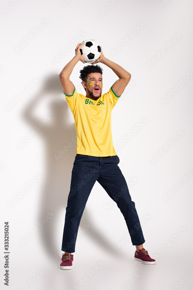excited african american football fan in yellow t-shirt holding ball on grey excited african american football fan in yellow t-shirt holding ball on grey