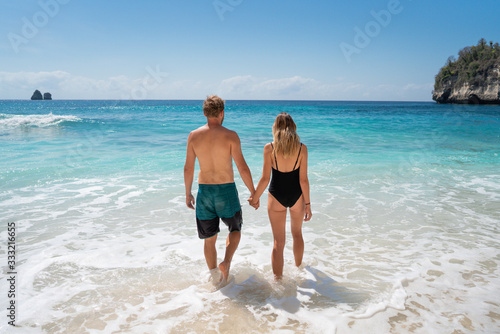 Happy young couple enters the ocean with turquoise clear water. Paradise vacation of a guy and a girl in Bali. Romantic holidays on the island of Nusa Penida, Bali
