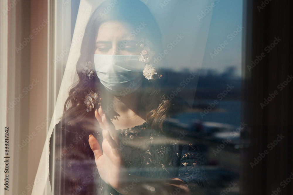 Fototapeta premium Young pretty woman in medical mask decorated with spring flowers stay isolation at home for self quarantine. Concept home quarantine, prevention COVID-19, Coronavirus outbreak situation