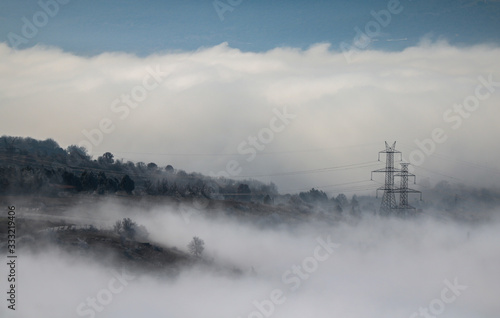 Foggy mountains for background. Electric pylon between mist and clouds. Forest at winter time.