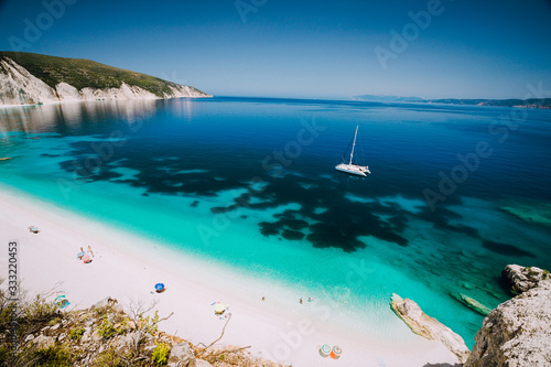 White catamaran yacht in clear blue sea water. Tourists on sandy beach near azure sea lagoon. Kefalonia, Greece