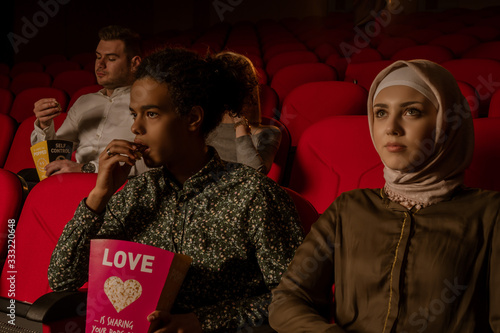 African american muslim man with his wife sitting in movie theater, watching movie, eating popcorn, smiling. © Infot