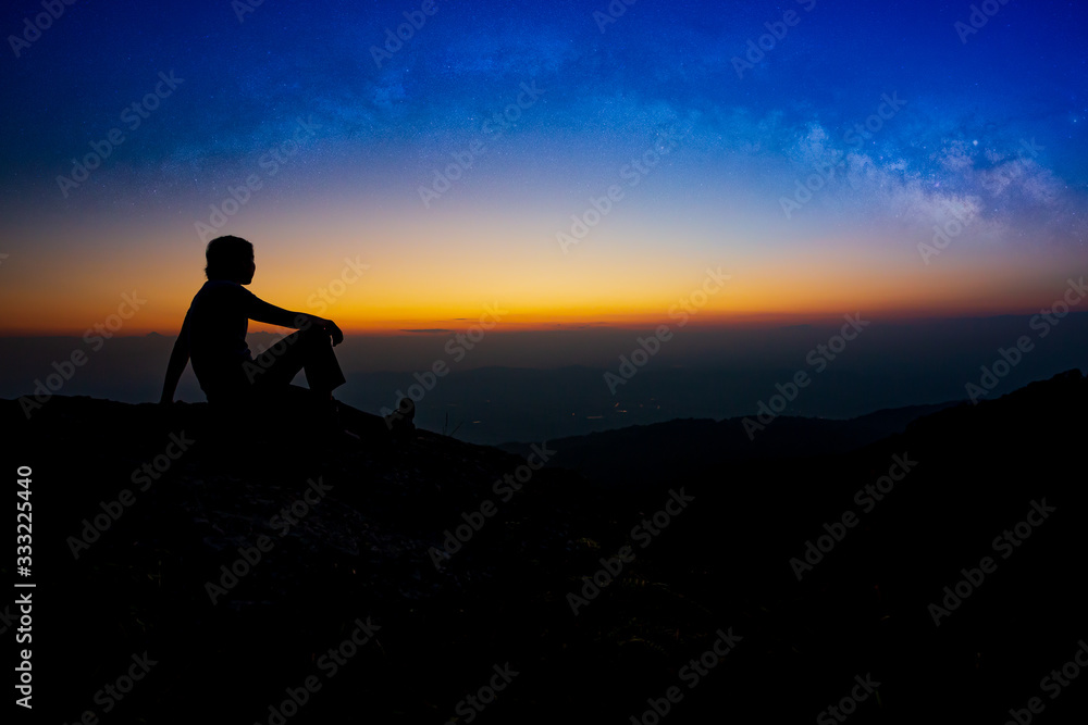 Man sitting on a rock looking at the stars with mountain landscape at night