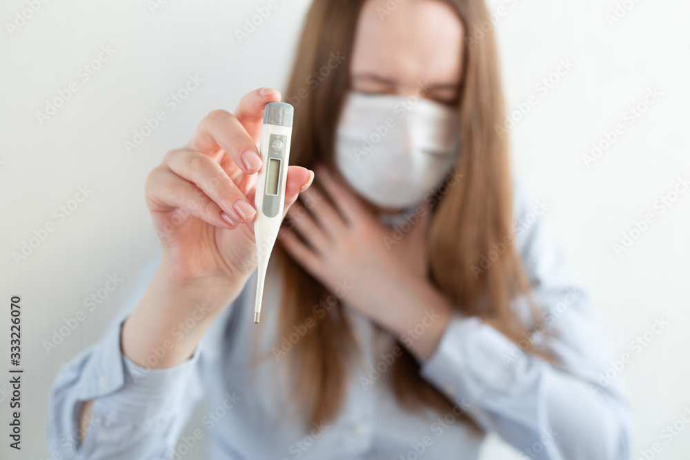 Woman in medical mask with thermometer in hand, with laptop, sitting on bed at home. Coronavirus. Business woman working from home wearing protective mask. Woman in medical mask with thermometer in hand, with laptop, sitting on bed at home. Coronavirus. Business woman working from home wearing protective mask.