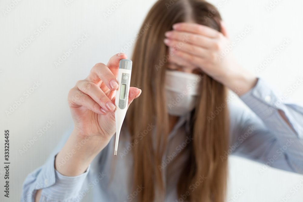 Woman in medical mask with thermometer in hand, with laptop, sitting on bed at home. Coronavirus. Business woman working from home wearing protective mask. Woman in medical mask with thermometer in hand, with laptop, sitting on bed at home. Coronavirus. Business woman working from home wearing protective mask.