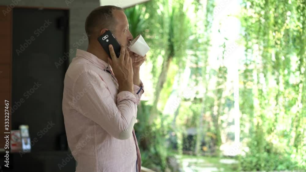 Young man talking on cellphone and drinking coffee at luxury home Young man talking on cellphone and drinking coffee at luxury home