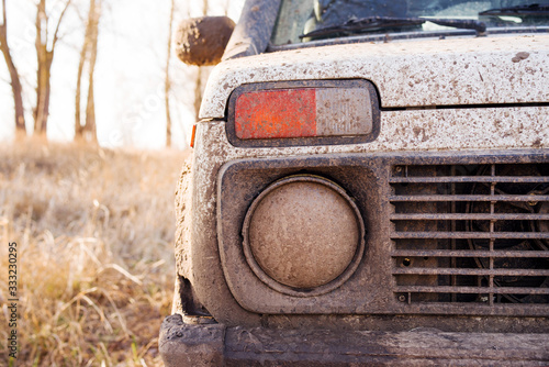 Headlight, grille and bumper of an SUV in mud closeup on the river bank