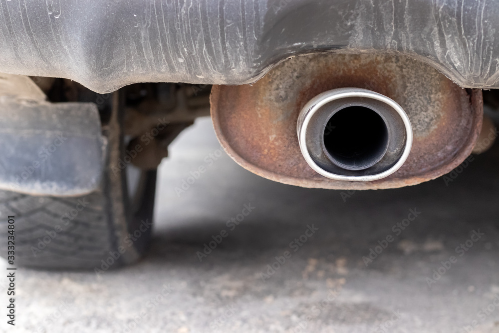 Rusty, dusty exhaust pipe of the car against a blurred background of the rear wheel. Closeup view. Selective focus Rusty, dusty exhaust pipe of the car against a blurred background of the rear wheel. Closeup view. Selective focus