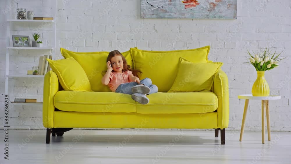 happy child talking on smartphone while sitting on sofa happy child talking on smartphone while sitting on sofa