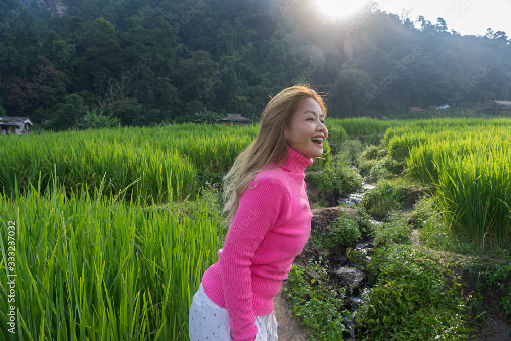 Asian woman in pink sweater smiling walking in rice field