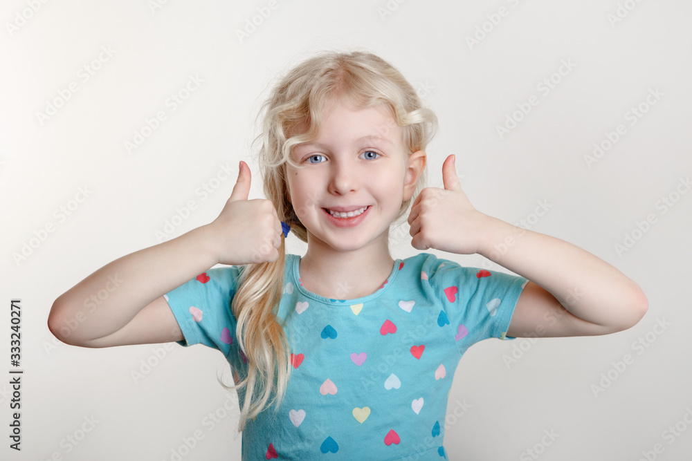 Portrait of beautiful little funny joyful blonde Caucasian girl on a light background. Happy smiling preschool child kid showing like thumb fingers. Positive emotion face expression. Portrait of beautiful little funny joyful blonde Caucasian girl on a light background. Happy smiling preschool child kid showing like thumb fingers. Positive emotion face expression.