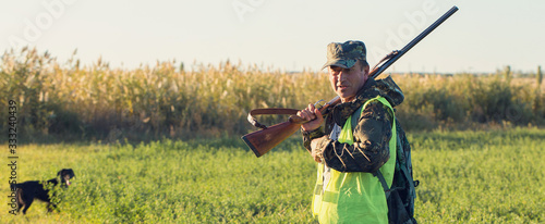 Hunter with a gun in his hands on the background of the steppe. Pheasant hunting in the early morning in the fall. Panoramic image, toned.