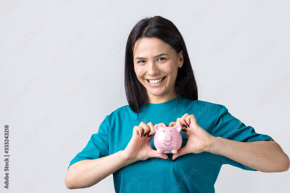 The girl holds a pink piggy bank and a coin in her hands. The concept of wealth and accumulation. The girl holds a pink piggy bank and a coin in her hands. The concept of wealth and accumulation.