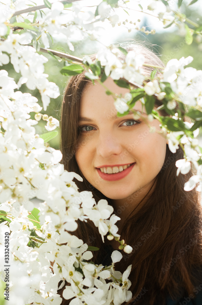 Fototapeta premium Portrait of a smiling girl with blue eyes in a blooming garden