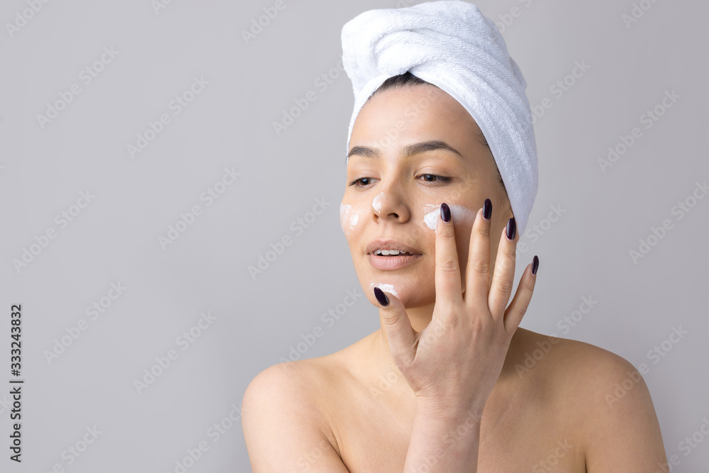 Beauty portrait of woman in white towel on head applies cream to the face. Skincare cleansing eco organic cosmetic spa relax concept. Beauty portrait of woman in white towel on head applies cream to the face. Skincare cleansing eco organic cosmetic spa relax concept.
