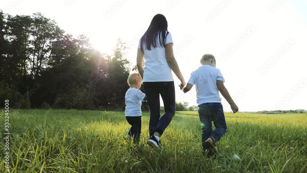 happy family teamwork mother, little brother and sister walk in the park nature holding hands slow motion video concept. mom, kids boy and girl daughter and son hold hands go on lifestyle green grass happy family teamwork mother, little brother and sister walk in the park nature holding hands slow motion video concept. mom, kids boy and girl daughter and son hold hands go on lifestyle green grass